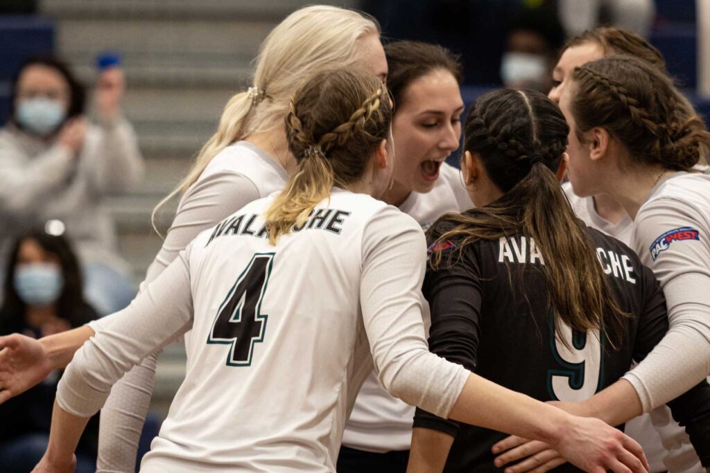 An image of five female volleyball players celebrating in a group huddle.