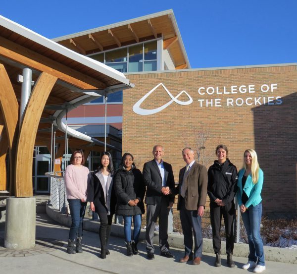 Image shows Columbia Basin Trust President & CEO Johnny Strilaeff and College of the Rockies President David Walls shaking hands, flanked by students.