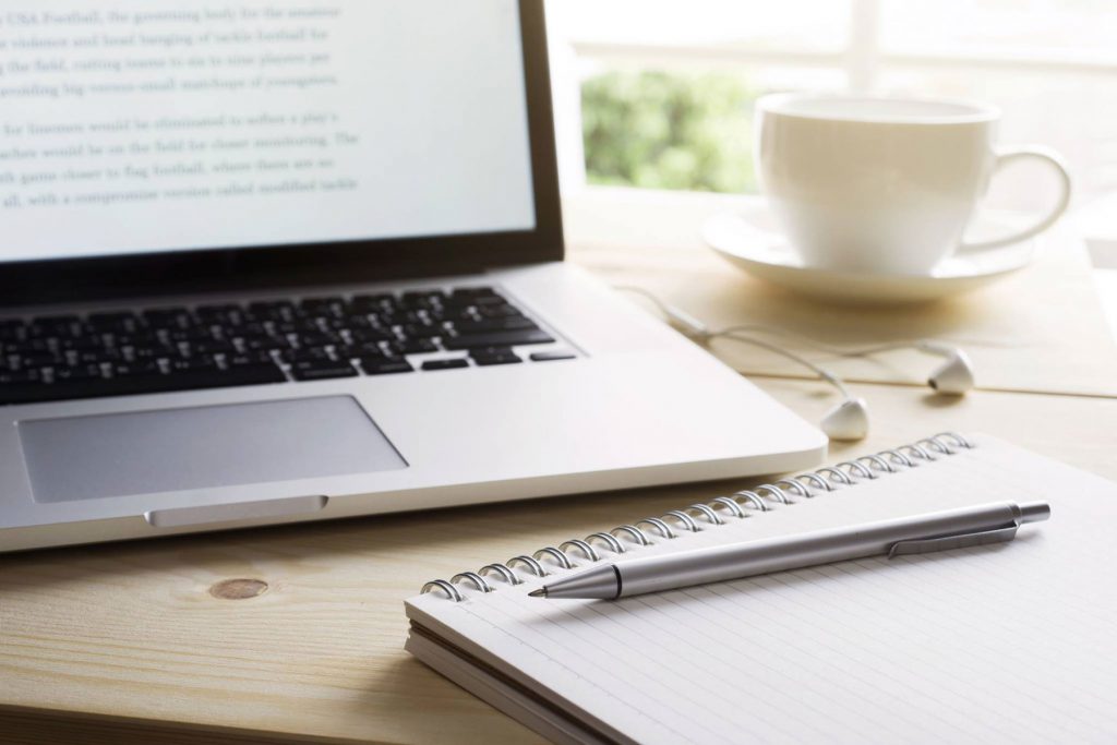 An image of a laptop computer and pad of paper with pen.