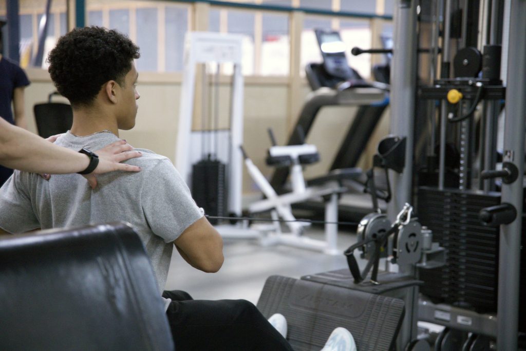 Kinesiology student helping classmate train on weight equipment.