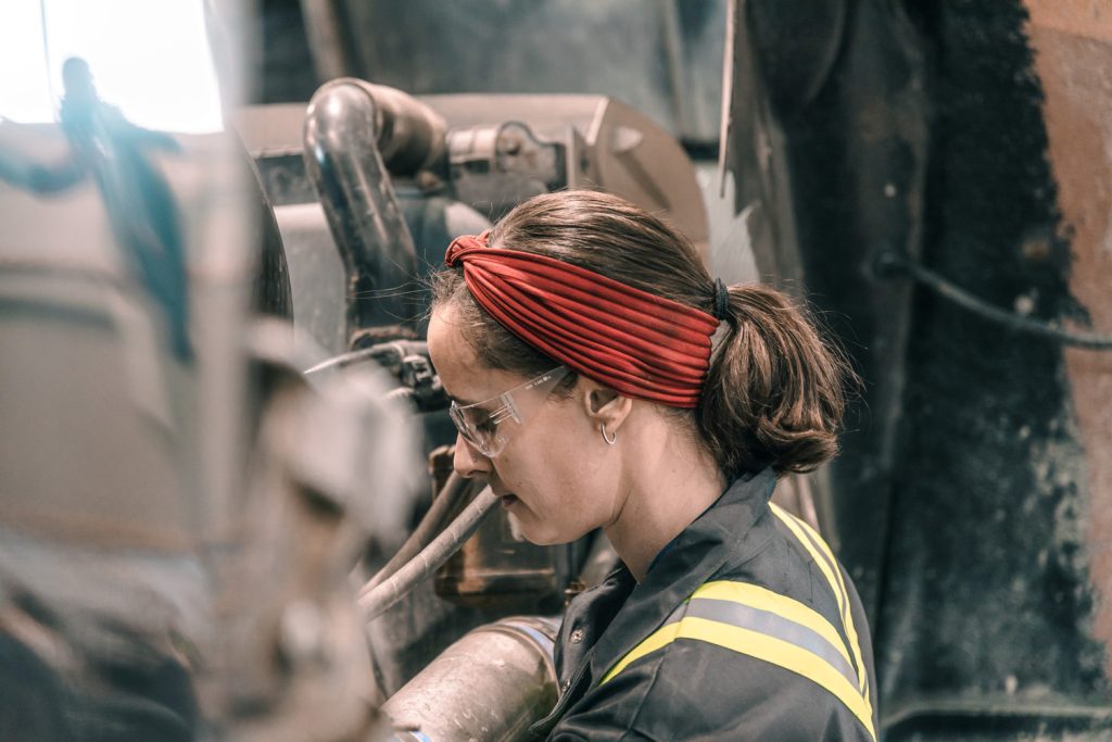 An image of a female heavy duty mechanic working on machinery.