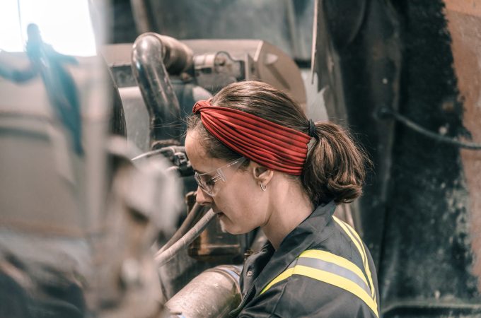 An image of a female heavy duty mechanic working on machinery.