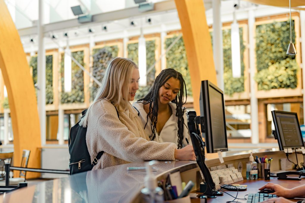 Two young female students inquiring at enrolment services desk.