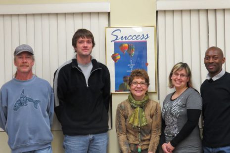 Image shows five individuals, three males and two females, standing in front of a poster that talks about success.
