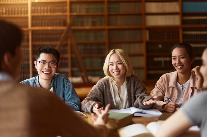 Team of happy Asian college students communicating while learning together in library.