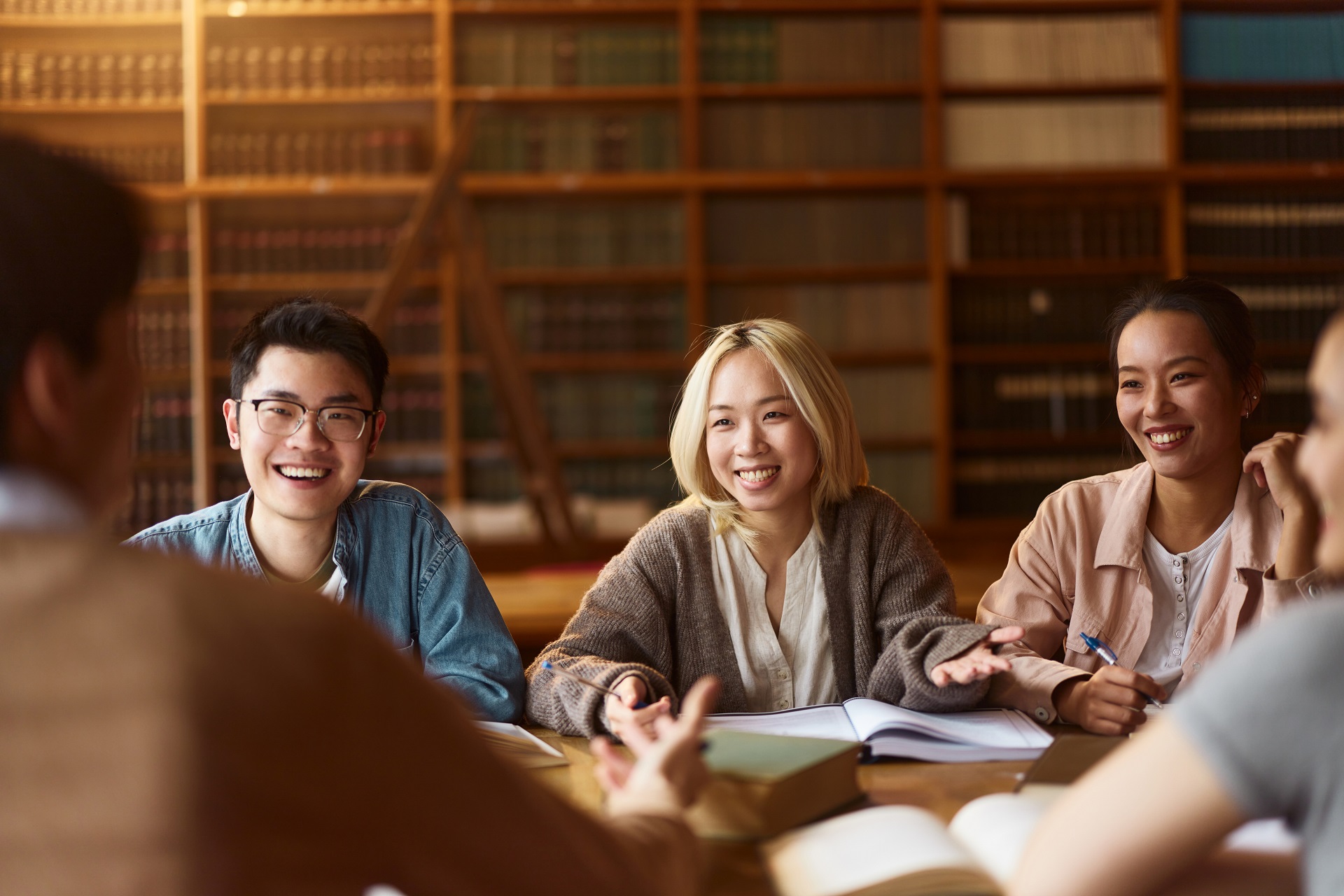 Team of happy Asian college students communicating while learning together in library.