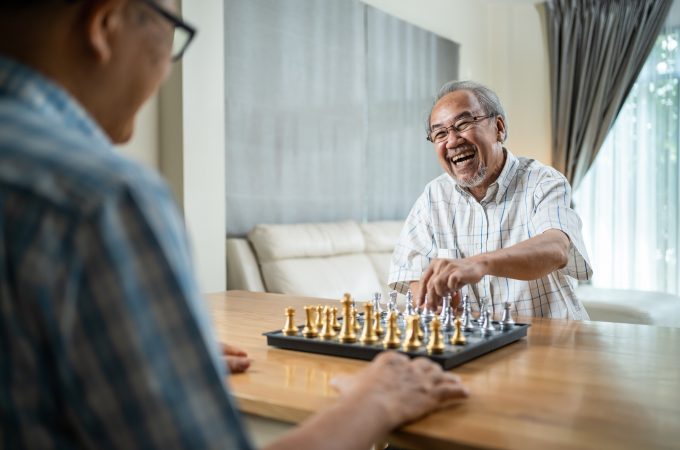Asian Senior Elderly male spend leisure time, stay home after retirement. Happy smiling Old man enjoy activity in house playing chess game with friend together. Hospital Healthcare and medical concept