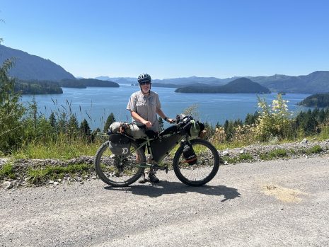 Image shows man with mountain bike standing near a lake