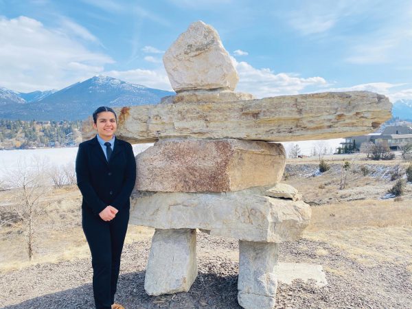 Image shows young woman in business suit standing next to a very large inukshuk
