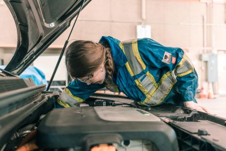 Image shows young woman working on the engine of a car.
