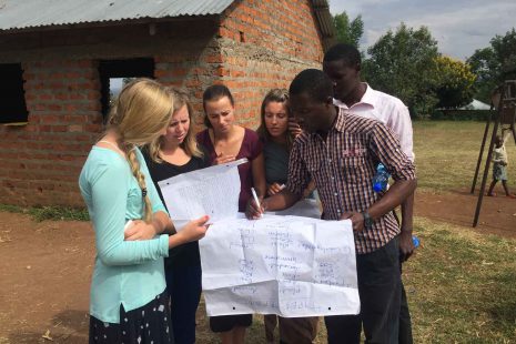 A photo of four nursing students studying a large piece of paper along with two locals from Kenya as one Kenyan writes on the paper.