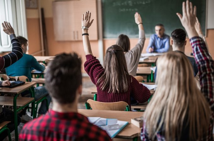 Students in the classroom raising hands to answer teacher's question.