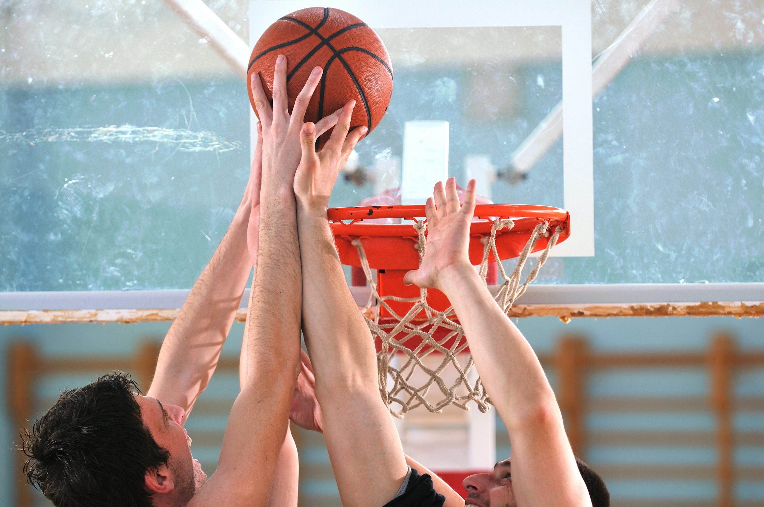 An image of two basketball players hands and a hoop and ball.