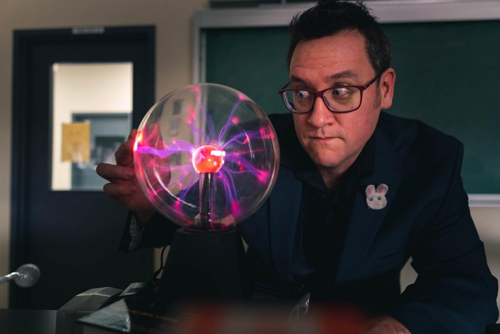 Image shows man in glasses looking at a plasma ball.