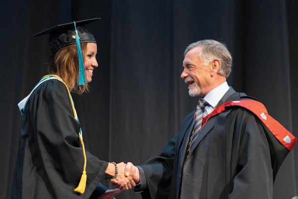 Image shows College of the Rockies President David Walls shaking the hand of Lieutenant Governor's Medal recipient Brenda Cortes Vargas during the 2019 commencement ceremony.