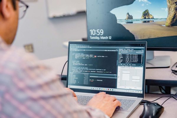 Image shows male student working with code on a laptop.