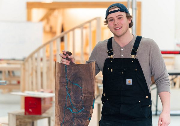 Image of man in Carhartt overalls and a backwards cap holding a completed charcuterie board.