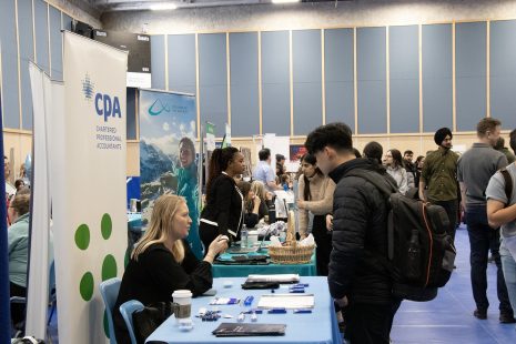Image shows job seekers gathered around booths, speaking to potential employers