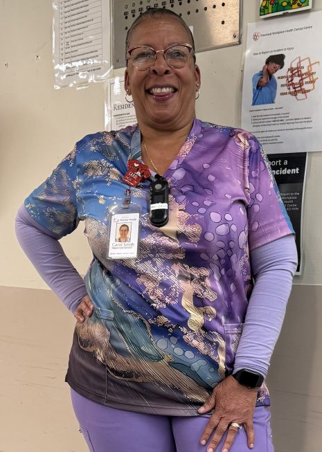 Image shows woman in colourful scrubs posing in a hallway.