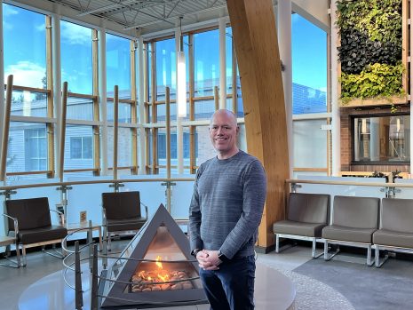 Image shows man standing next to a fireplace.