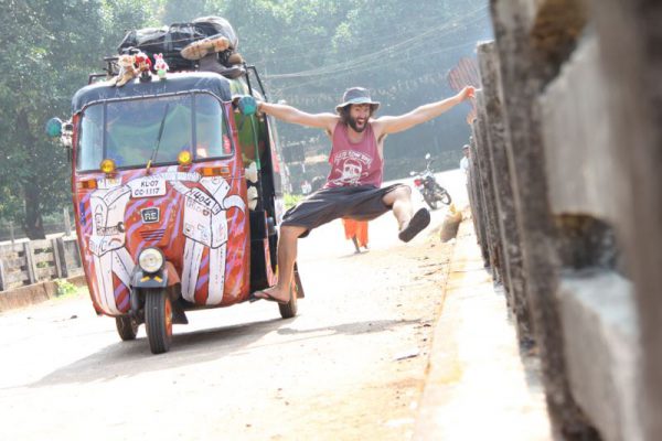 Image of man jumping with apparent glee alongside a rickshaw in India.