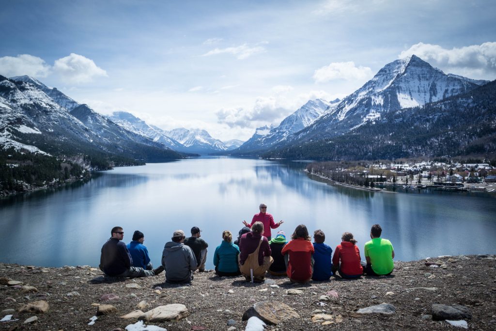 Group of Students sitting in front of instructor with mountains and lake in background.