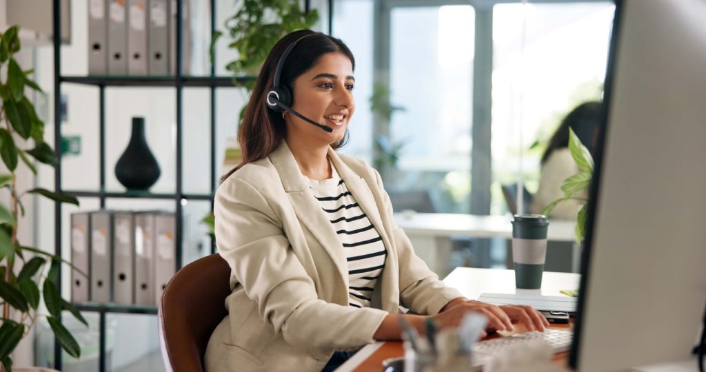 Office admin sitting at computer, wearing a headset.