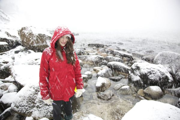 Image of woman in red jacket standing on rocks during a snow storm.