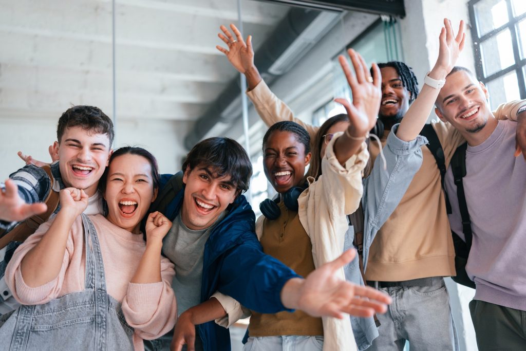A cheerful group of diverse students joyfully posing and celebrating in an open, modern setting.