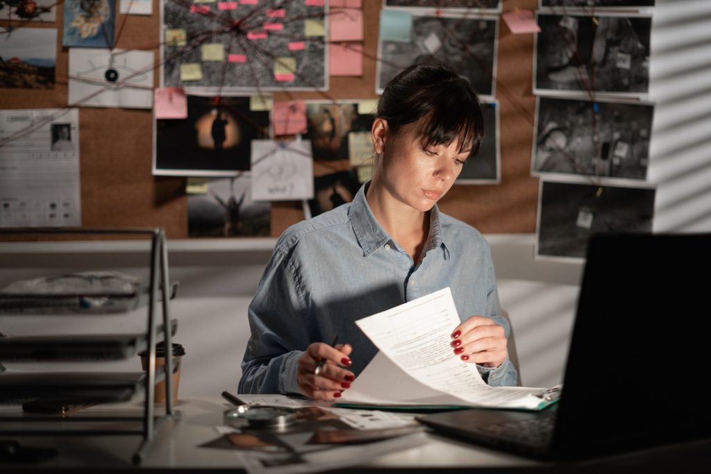 Female Detective processing evidence in office using laptop computer at night. Copy space