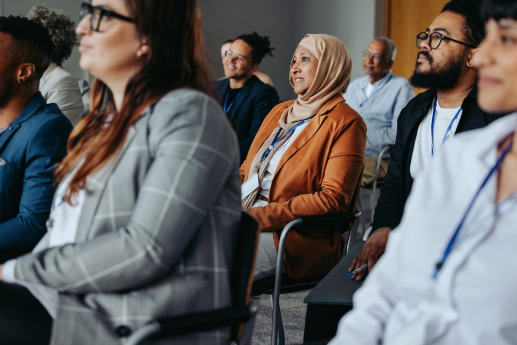 Businesswoman wearing hijab attentively listening during a conference presentation, surrounded by diverse colleagues.