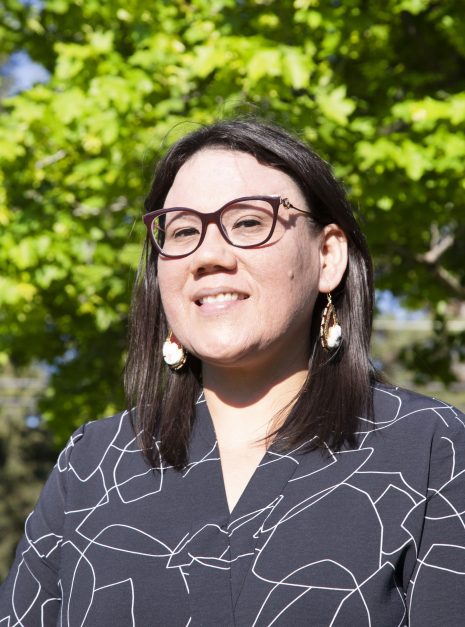Image shows woman in glasses standing outside and smiling at the camera.
