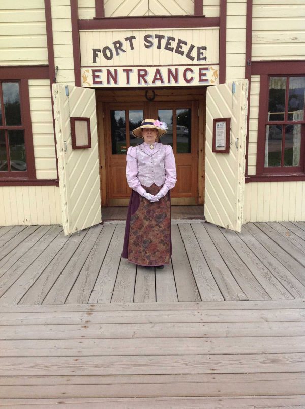 Image of woman in period clothing in front of the entrance to Fort Steele Heritage Town.