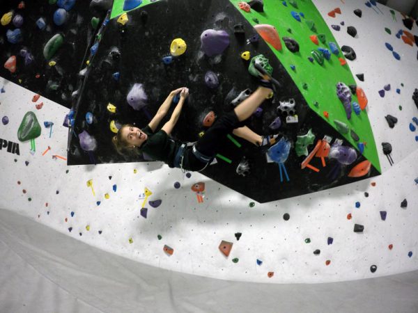 Image of young woman hanging from climbing wall.