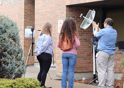 image shows man adjusting a satellite with two people looking on