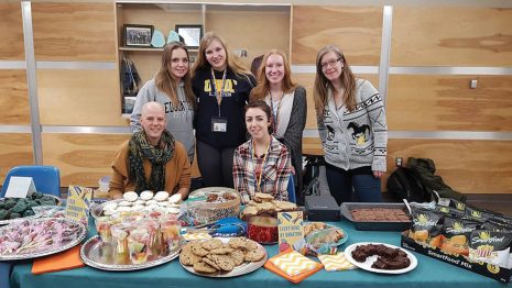 Image shows group of Education Students' Association - Cranbrook Division members sitting behind a table filled with baked goods.