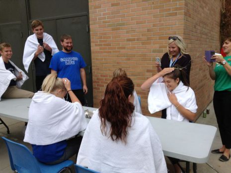 Image shows two female students smashing eggs on their heads while other students and staff look on.