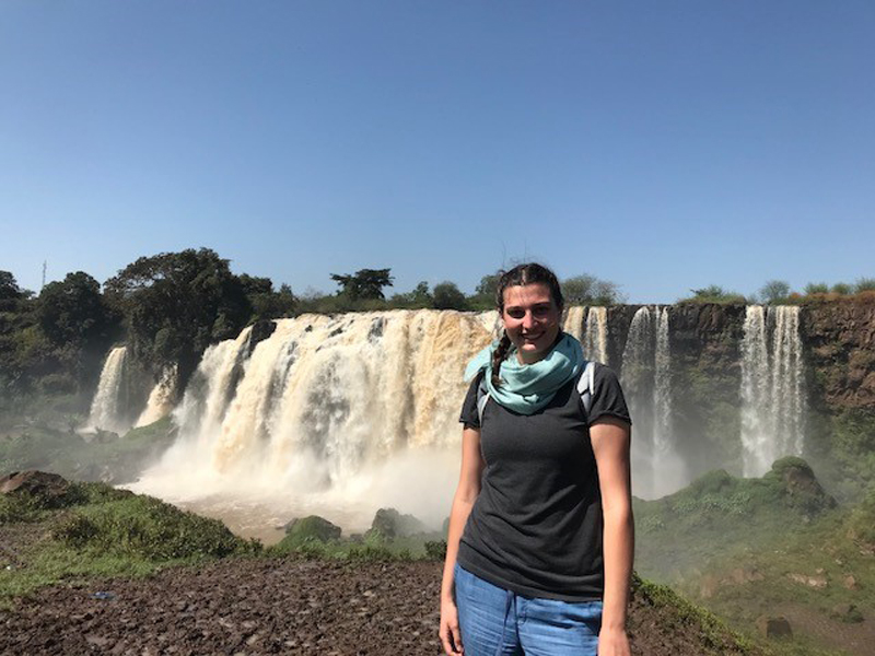 Image of young woman with Kenyan waterfall behind her.