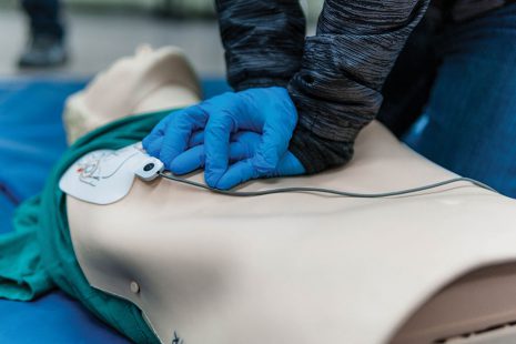 Image shows gloved hands performing compressions on a first aid mannequin