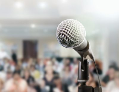 Audience sits waiting for the speaker at a conference. The microphone is in the foreground.