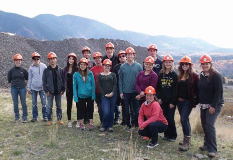 Image shows a group of young people with hardhats standing in front of large pile of rock and dirt.