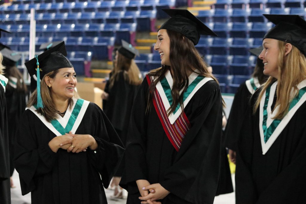 Three female graduate students smiling and chatting at a Convocation ceremony.