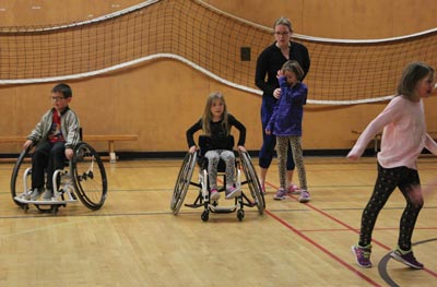 Image shows young children playing in a gymnasium, two in wheelchairs.