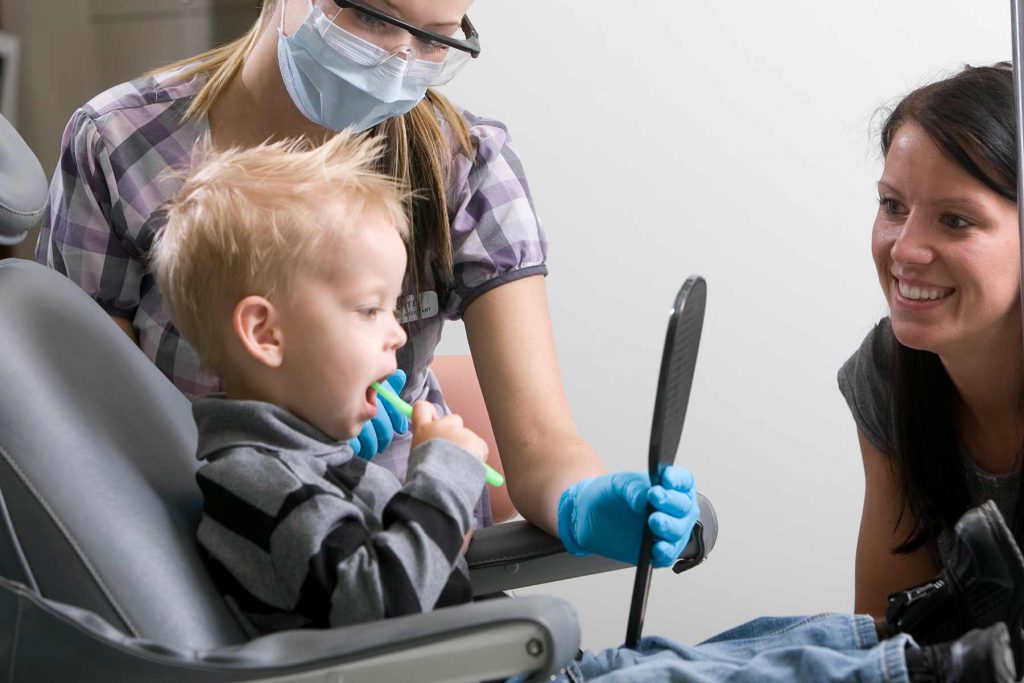 Dental Assistant student holding mirror for young toddler.