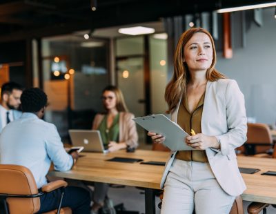 Portrait of beautiful smiling businesswoman with her colleagues during a meeting in office board room. Successful team leader and her team working in background.