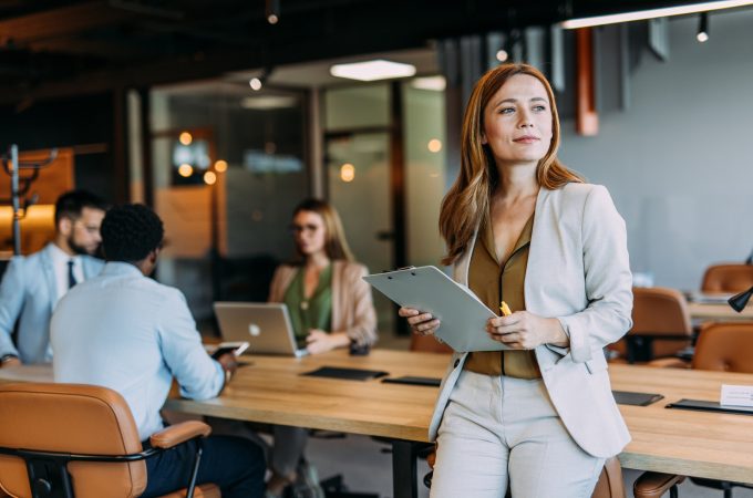 Portrait of beautiful smiling businesswoman with her colleagues during a meeting in office board room. Successful team leader and her team working in background.