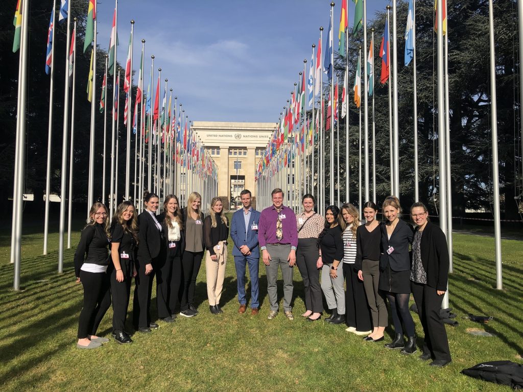 A group of nursing students outside the Geneva UN building with nations flags in the background.