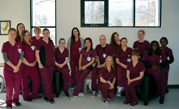 Image shows group of students and staff in maroon scrubs, smiling at the camera