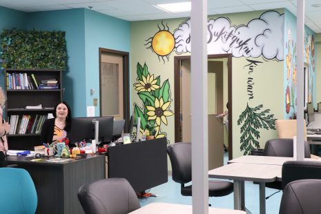 Image shows woman sitting in the newly remodeled Learning Commons with a colourful Indigenous mural on the wall behind her.