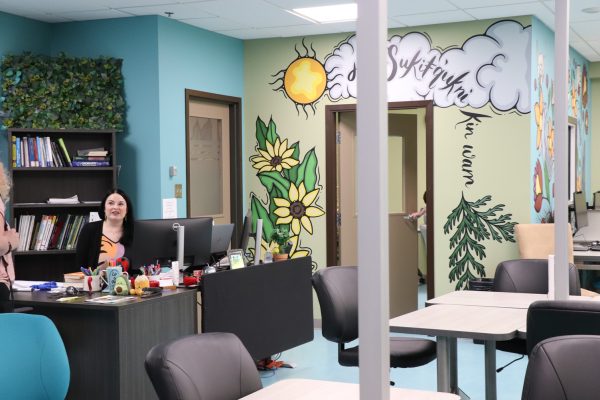 Image shows woman sitting in the newly remodeled Learning Commons with a colourful Indigenous mural on the wall behind her.